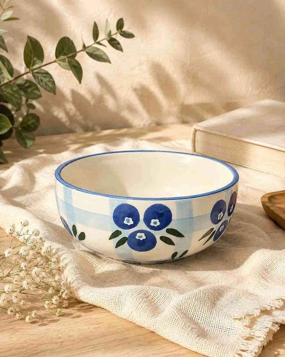 A white bowl painted with blueberries on a blue gingham band